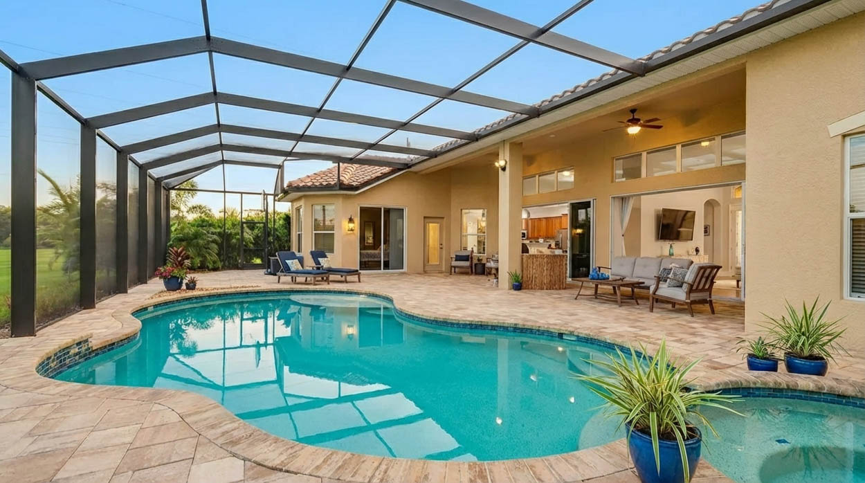 Dark-framed pool screen enclosure over a freeform pool and spa, with a paver deck, loungers and an open lanai.