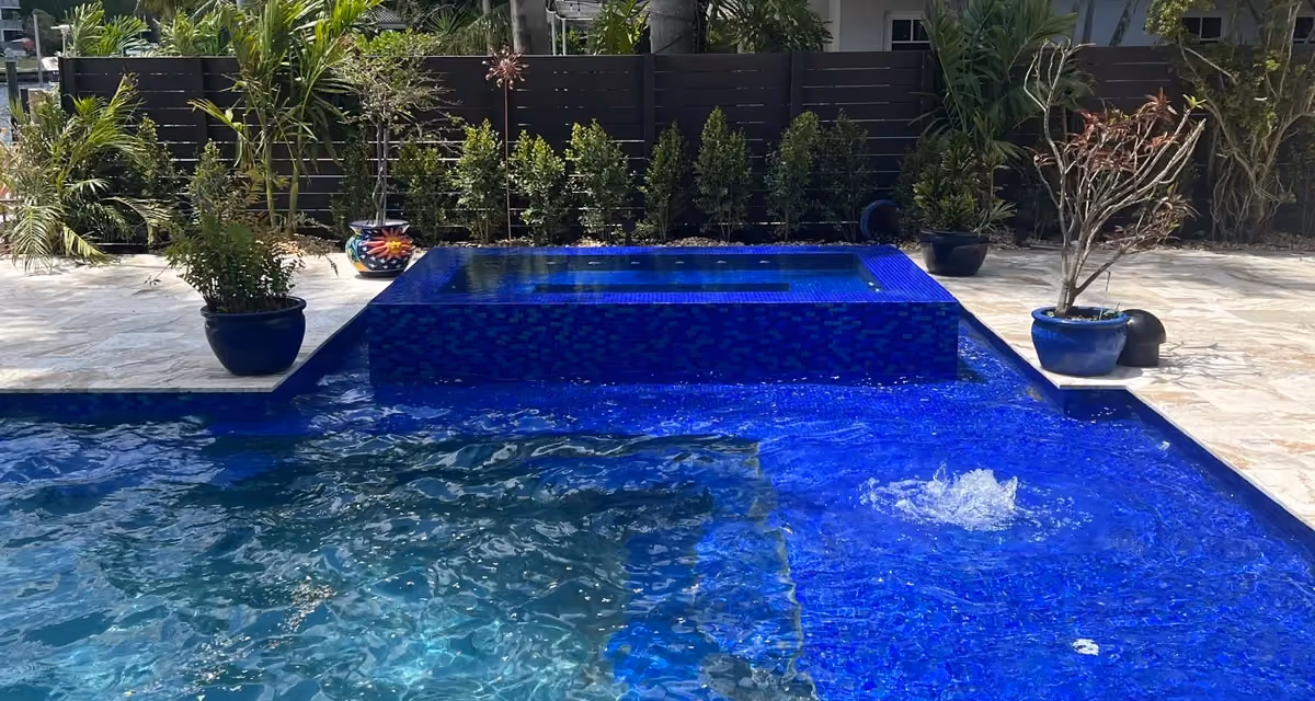 Pool with cobalt glass mosaic sun shelf, two bubblers and a raised tiled spa framed by royal palms.