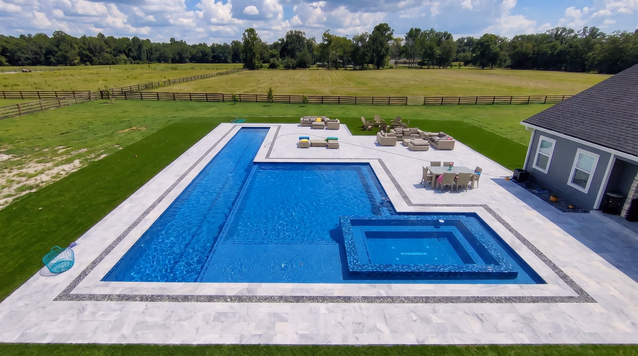 Large geometric pool with a sun shelf and raised spa on an open lot, framed by a banded marble deck.