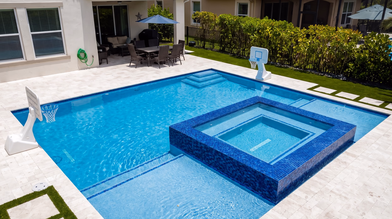 Rectangular pool with a raised blue glass mosaic spa spilling into the water, framed by a travertine paver deck.