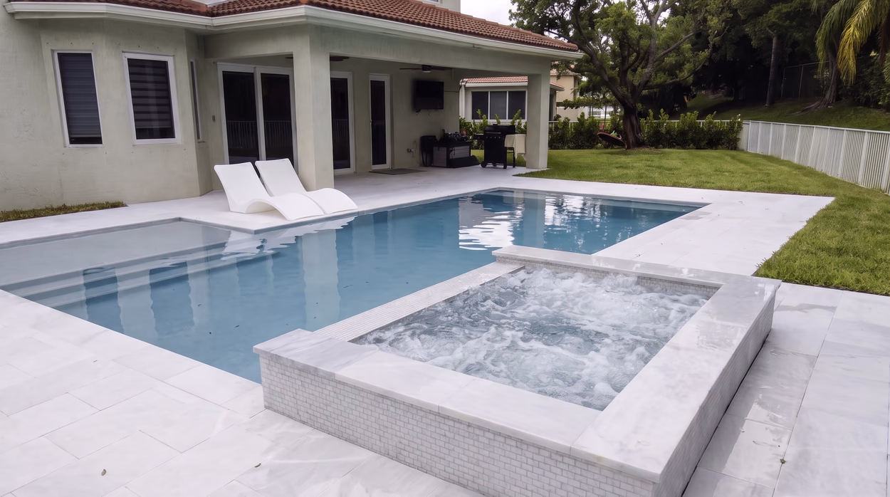 Pool with a raised white-tiled spa in the foreground and the covered lanai of the home behind.
