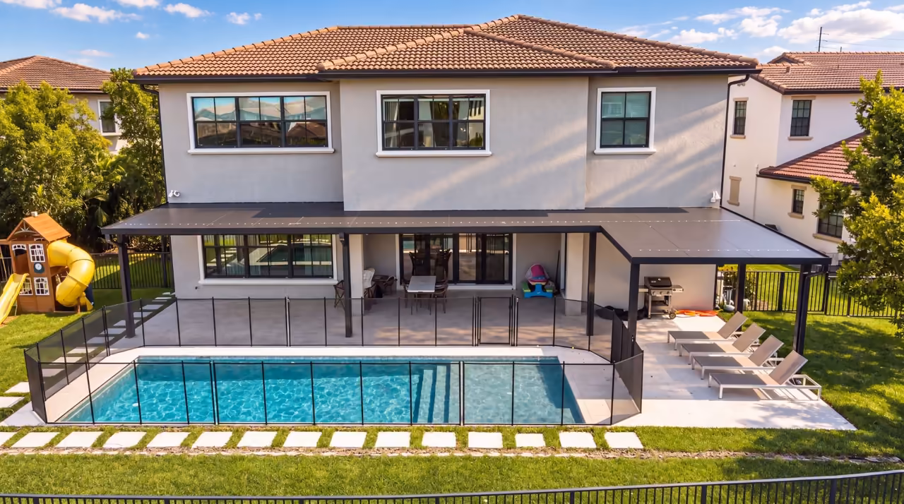 Same backyard after renovation: black louvered pergola, lap pool and travertine pool deck with lounge chairs