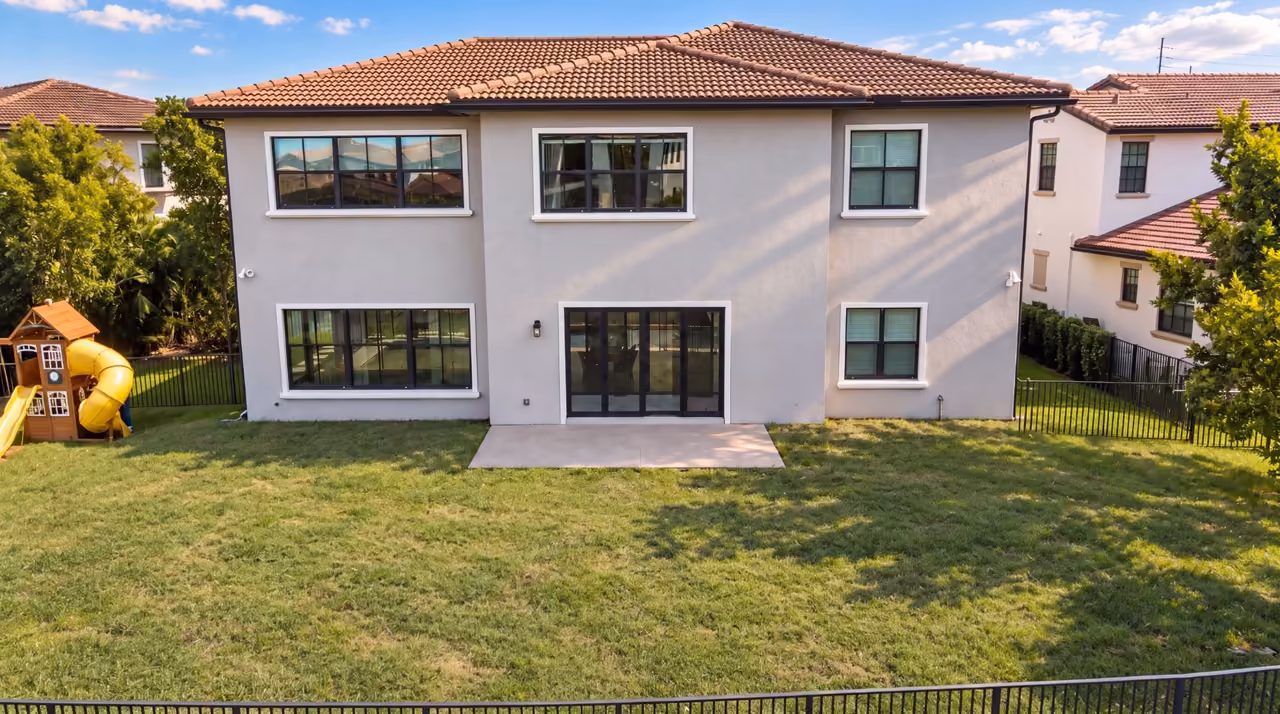 Backyard before renovation: empty lawn and a small concrete patio behind a two-story Florida home